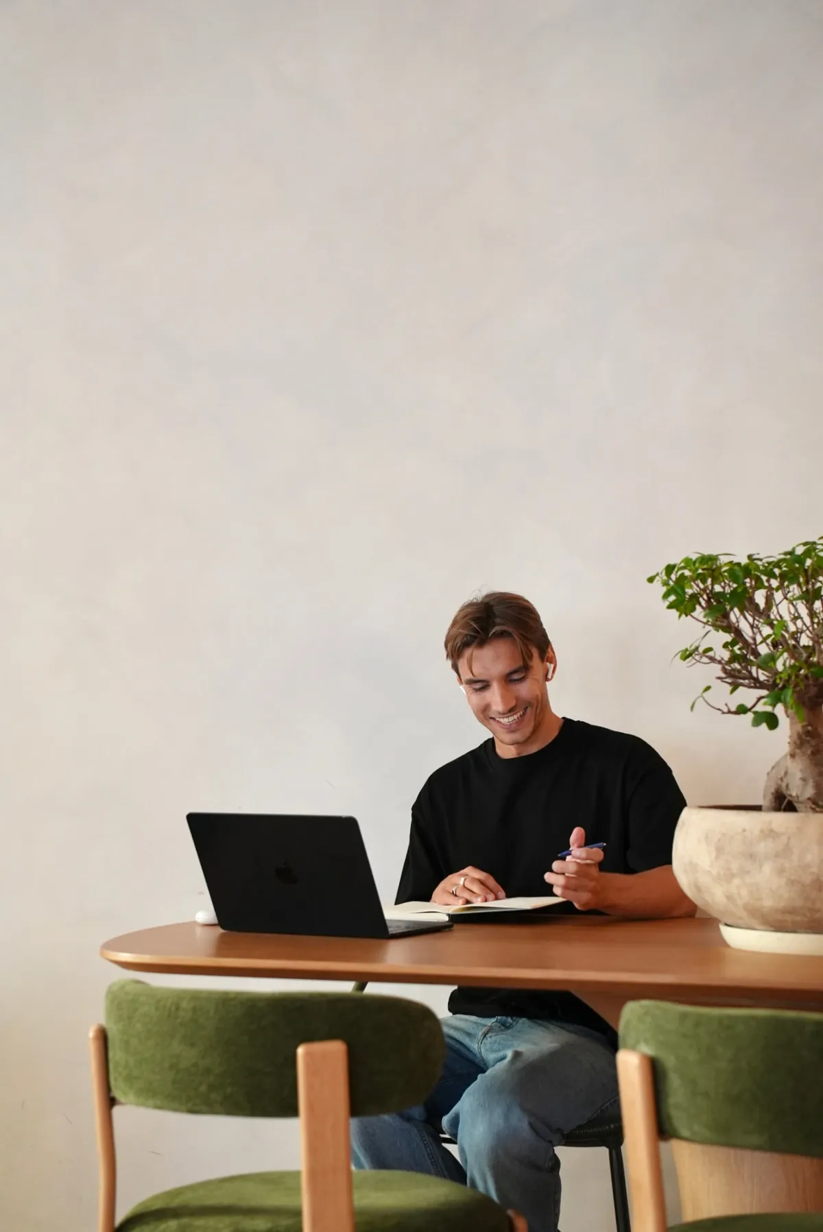 Julian Drachenberg sitzt lächelnd am Schreibtisch mit Laptop und Notizbuch